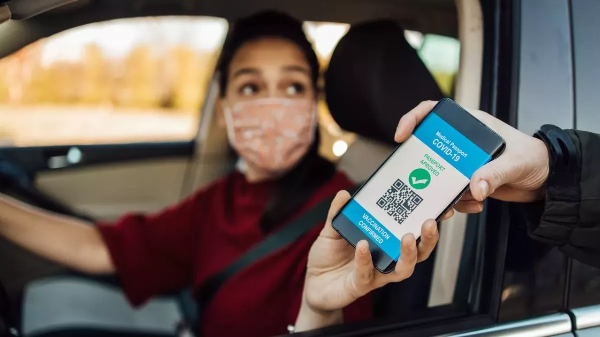Eine Frau am Steuer zeigt einem Beamten ein digitales Impfzertifikat auf ihrem Smartphone 
