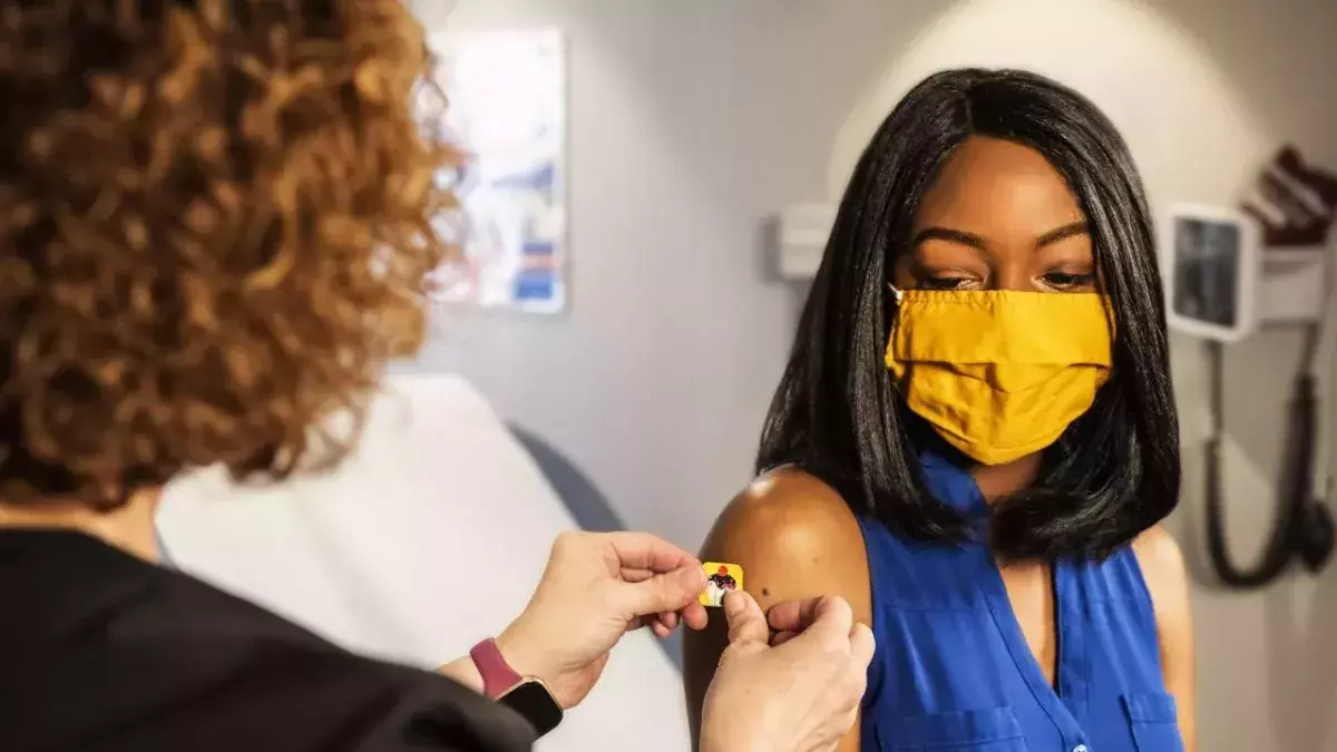 Eine schwarze Frau mit gelber Maske bekommt nach einer Impfung einen Pflaster aufgeklebt