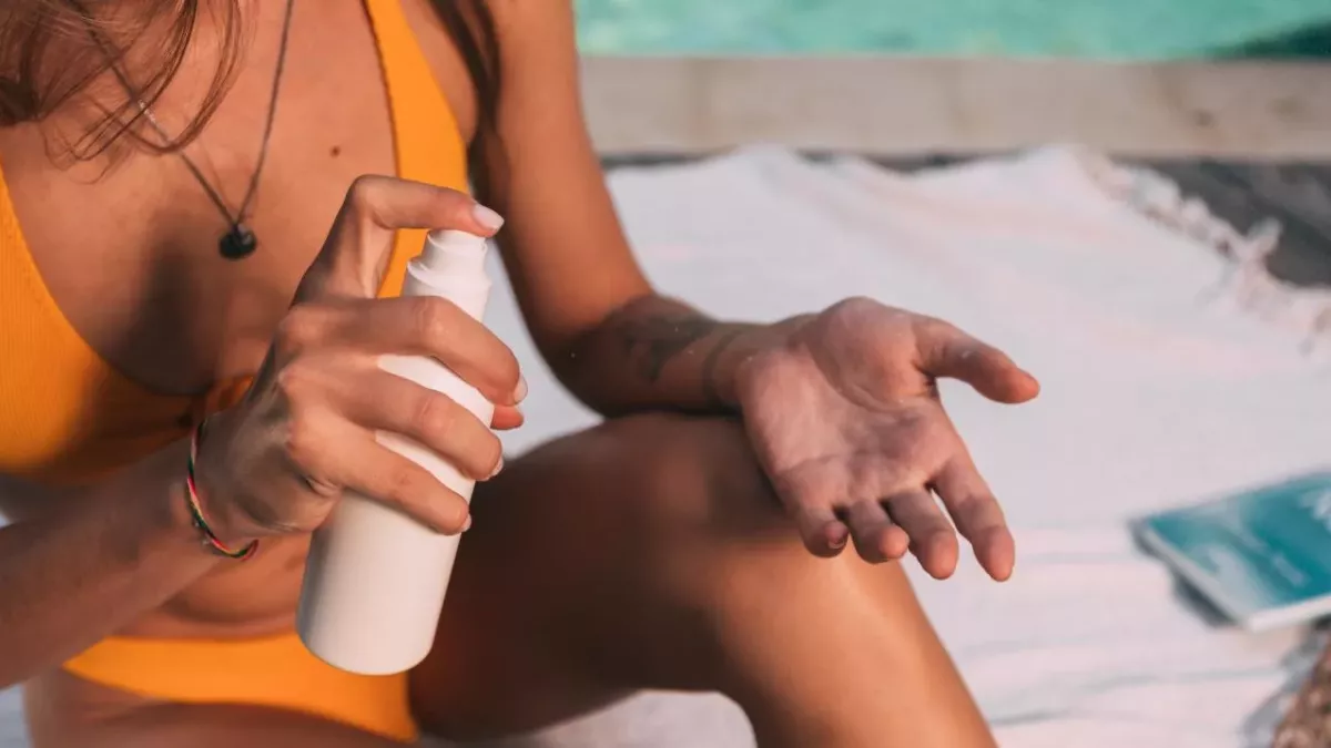 Eine Frau im gelben Bikini sprüht sich mit Sonnenschutz ein
