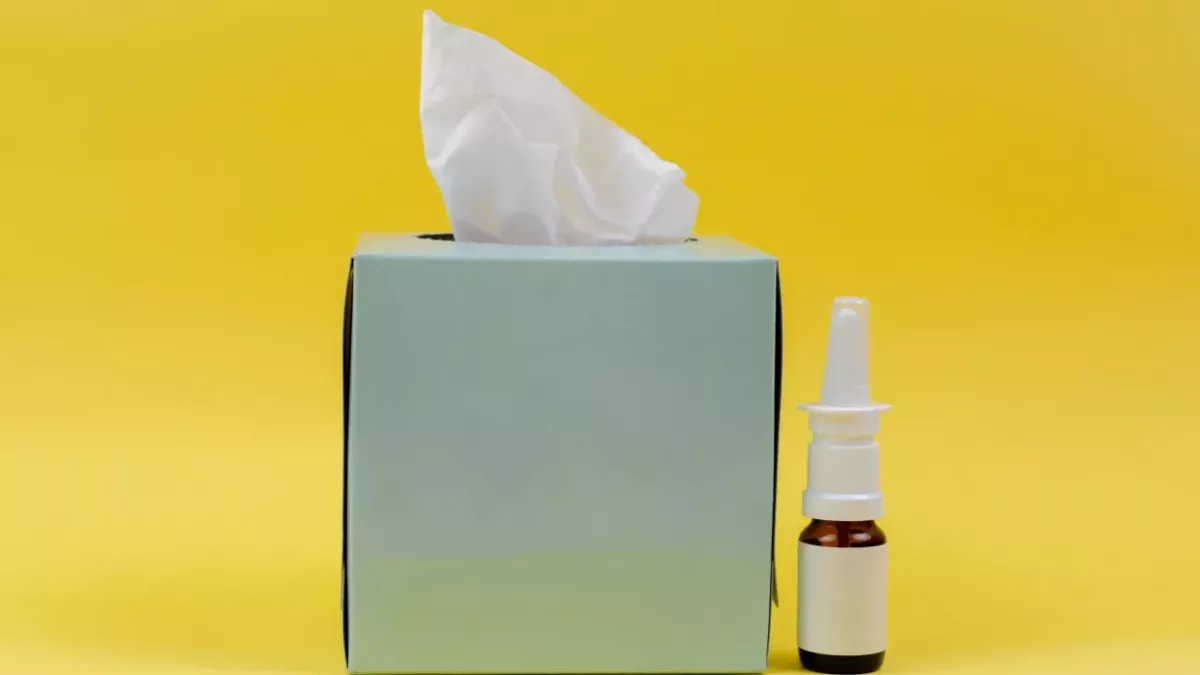 Eine Packung Taschentücher und ein Nasenspray vor gelbem Hintergrund